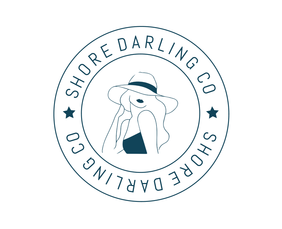 Minimalist logo of a woman in a sunhat and swimsuit, framed by two concentric circles with the text “SHORE DARLING CO” repeated and a star on each side.