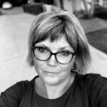 A black-and-white portrait of a woman with short hair wearing glasses and looking toward the camera. A black-and-white portrait of a woman with short hair wearing glasses and looking toward the camera.
